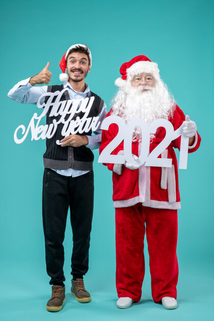 前面圣诞老人的正面图 蓝色墙壁上有人拿着新年快乐和2021年的木板快乐举行庆祝