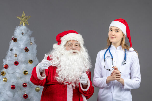 庆祝圣诞老人和年轻女医生在灰色墙壁上的正视图医疗服装听诊器