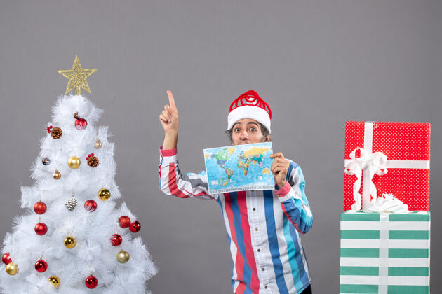 圣诞老人正面图惊讶的男子拿着螺旋弹簧圣诞帽拿着世界地图指着高处指向惊讶的人高