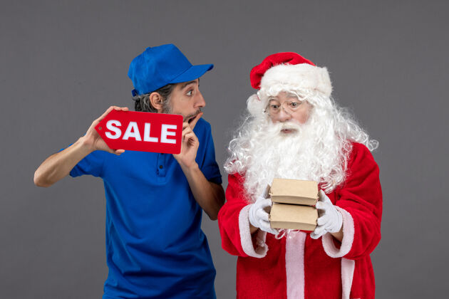 帽子圣诞老人的正面图 男信使手持销售横幅 灰色墙上有食品包装男人包裹地板