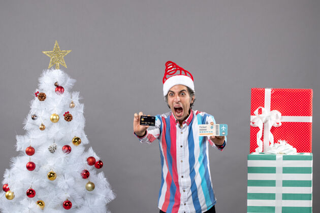 人前视图：手持卡片和旅行票的男子在圣诞树周围大声喊道 并赠送礼物旅行专业手持
