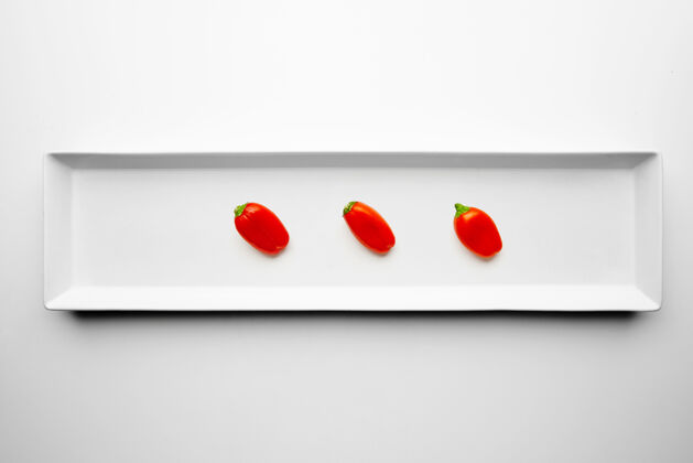 美味三个红辣椒隔离在白色背景上的矩形陶瓷板的中心切块成分食物