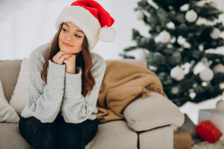礼物坐在圣诞树旁沙发上的年轻女子红色毛衣十二月盒子