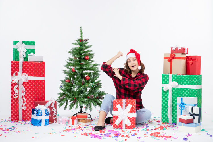庆祝年轻女子围坐在礼物和白色墙上的小圣诞树前的视图节日女人冬青