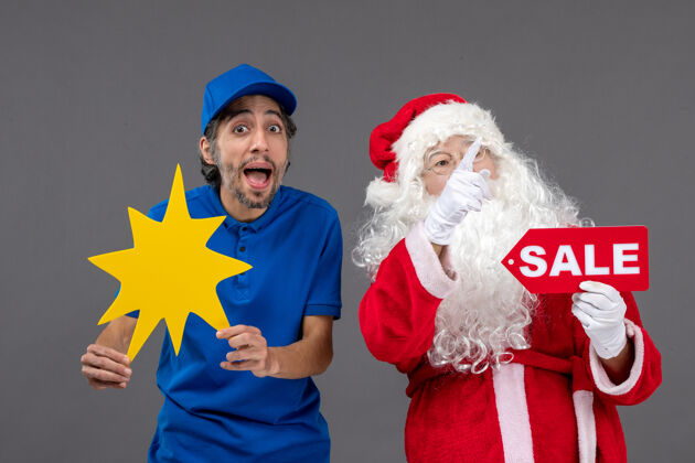 销售圣诞老人的正面图 男性信使手持销售横幅 灰色墙上有黄色标志快乐快乐圣诞老人