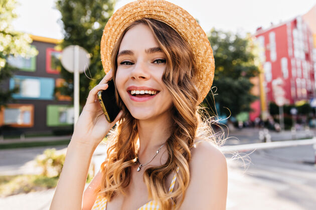 快乐夏日里 幽默的白人女孩在打电话街上戴着帽子拿着智能手机的漂亮女士的户外肖像人散步波浪发
