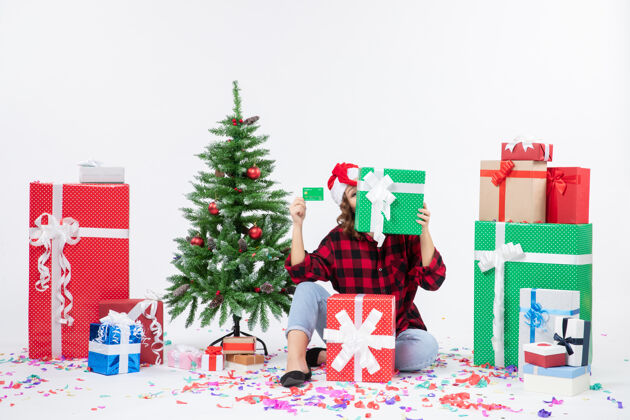节日正面图：年轻女子手持绿色银行卡和白墙上的礼物围坐在一起快乐抱着圣诞节