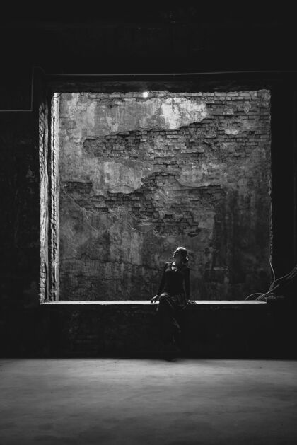 黑暗黑与白的看法孤独的女人坐在大窗户在旧的肮脏的建筑女人单色孤独