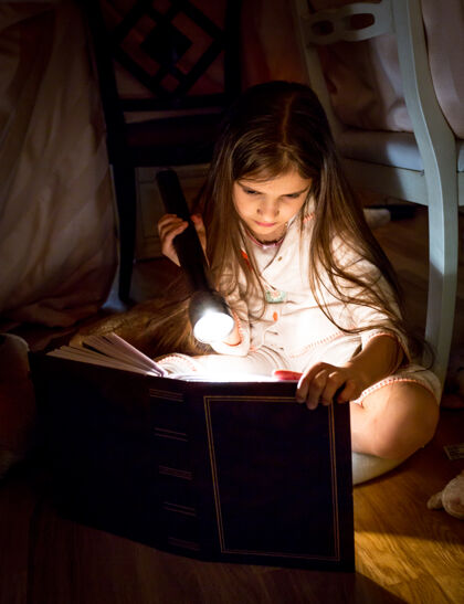 就寝时间可爱的小女孩晚上在毯子下看书手电筒童年故事