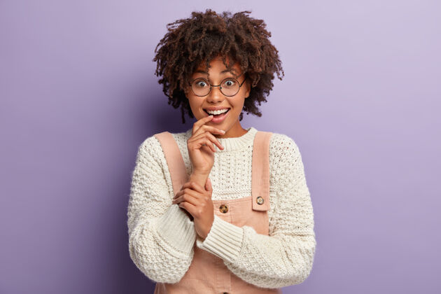 工作服可爱快乐的美国黑人年轻女子头像出席派对 穿着时髦的衣服 神情饶有兴趣 隔着紫色的墙壁 被可爱的礼物所打动好笑兴趣享受