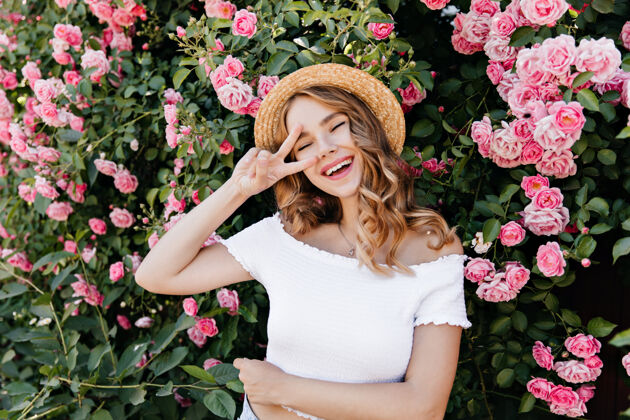 花园无忧无虑的金发女孩在花园里摆姿势大笑可爱的戴着玫瑰帽子的女人的户外肖像花植物享受