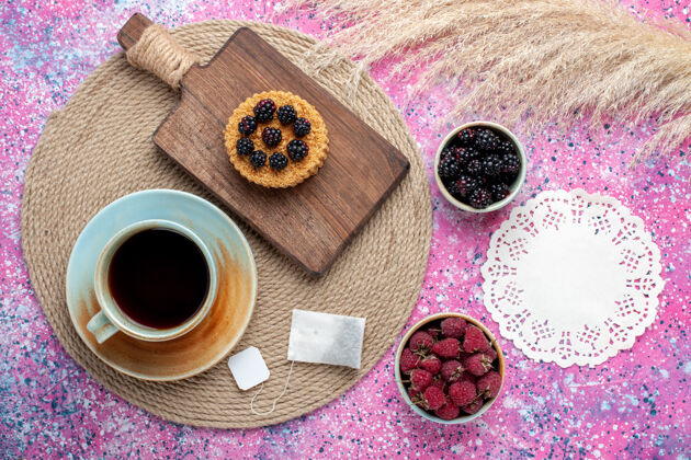 食物顶视图的小蛋糕与不同的浆果和茶杯上的粉红色表面浆果烘焙粉