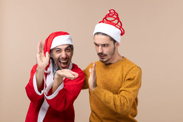 鼓掌正面图两个戴着圣诞帽的男人在米色孤立的背景上拍手帽子帽子微笑