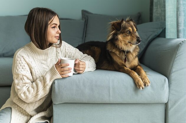 Covid19大流行期间 一个女人在家里的狗旁边喝咖啡防护女性社会距离