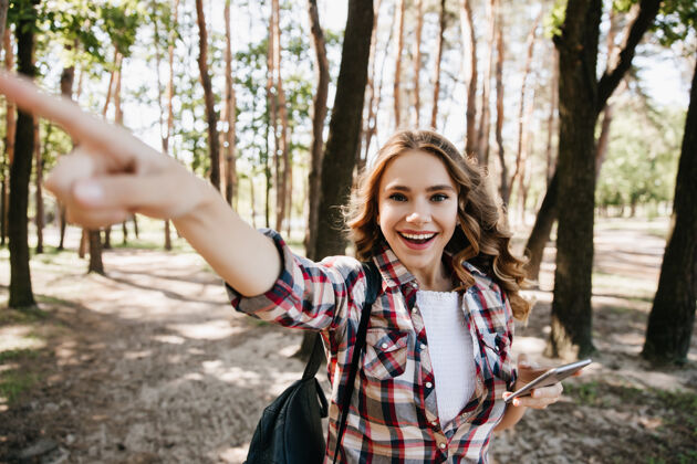 快乐兴奋的卷发女孩在森林中寻找正确的道路带着背包的情绪化女游客的户外写真周末开朗乐趣