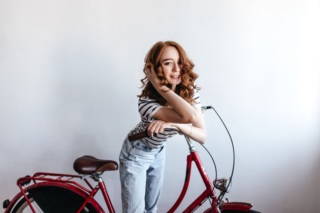 乐趣一位优雅的红发女士站在自行车旁拍照室内的卷发女孩穿着蓝色牛仔裤的肖像人自行车肖像