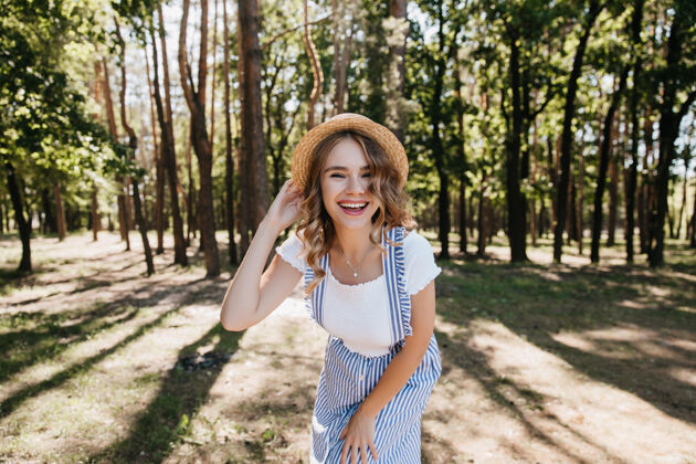 夏天在森林里拍照时 穿着时髦服装的漂亮女孩微笑着戴着帽子的可爱女模特在公园里享受美好的一天肖像成人无忧无虑