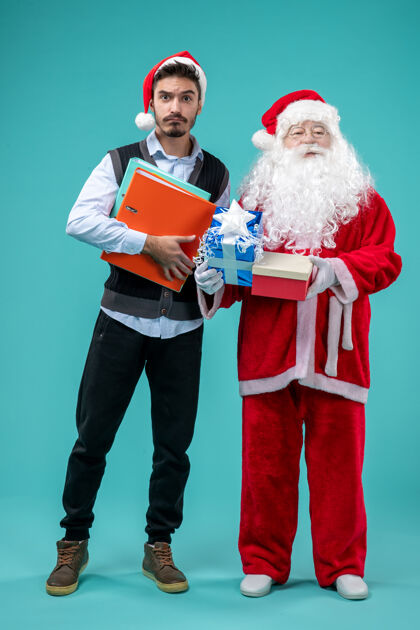 男人圣诞老人与年轻男性和礼物在蓝色墙上的正面视图假期节日圣诞