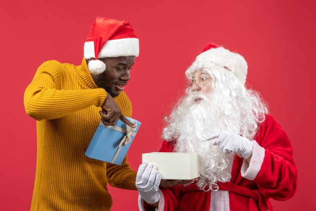 十二月圣诞老人和年轻人在红墙上打开礼物的正面视图年轻圣诞老人正面