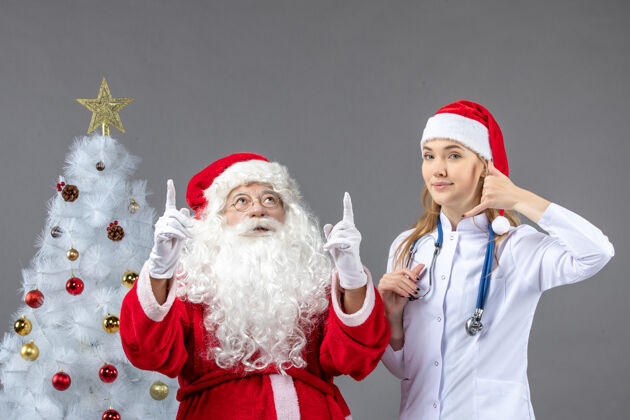 节日圣诞老人和年轻女医生在灰色墙壁上的正视图正面快乐圣诞老人