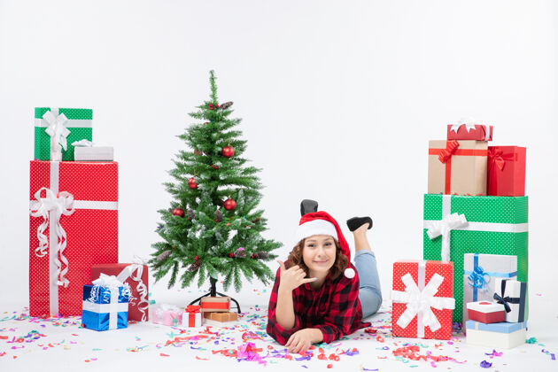 寒冷年轻女子躺在白色墙壁上的圣诞礼物和小圣诞树周围的正视图圣诞树礼物圣诞