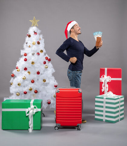 肌肉满意的男人拿着旅行票站在侧视图上 展示灰色的手臂肌肉购物圣诞树举行