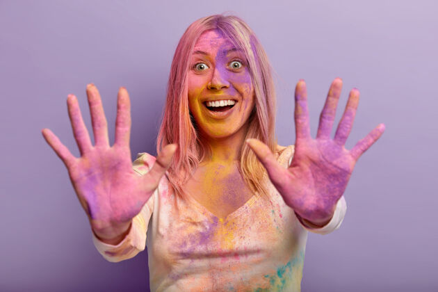 粉末喜笑颜开的年轻女子舒展着涂着彩色干粉的双掌 开心的表情 在胡里节和朋友们一起玩乐 与世隔绝的紫色墙壁室内手势满意