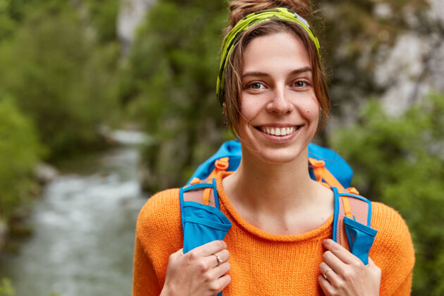 山一个穿着橙色套头衫 在绿色森林的小溪边散步的快乐的女游客的特写镜头自由自然姿势