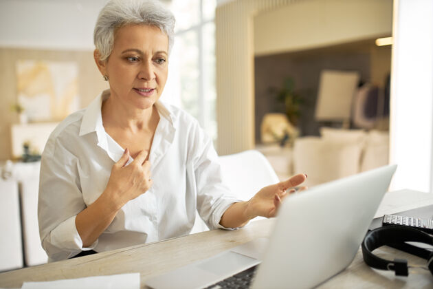 工作时尚成熟的女商人 留着短发 坐在笔记本电脑前 张着嘴看着屏幕 好像在说什么在线工作现代