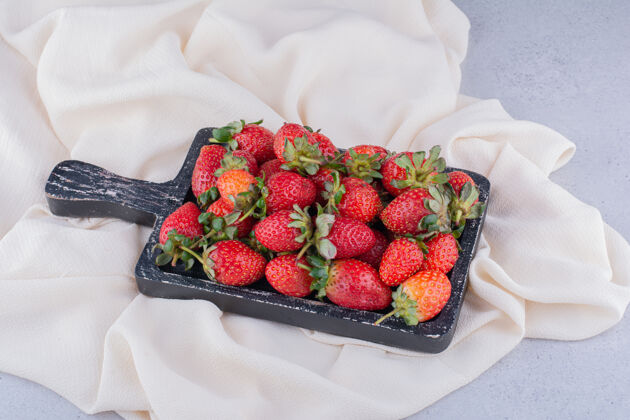 健康白色织物上的破旧托盘 大理石背景上有一堆草莓面料美味水果