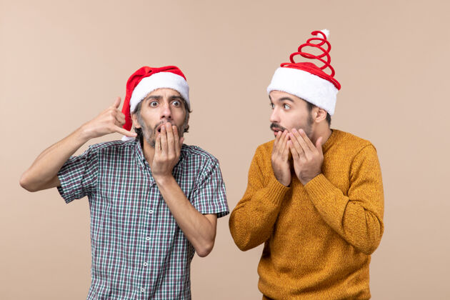管乐器正面图：两个奇怪的家伙在米色的孤立背景下戴着圣诞帽 非常惊讶家伙乐器男人
