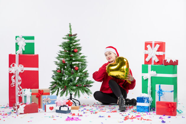 礼物正面图：年轻女子围坐在白色的墙上 手里拿着金色的心形礼物前面圣诞礼物