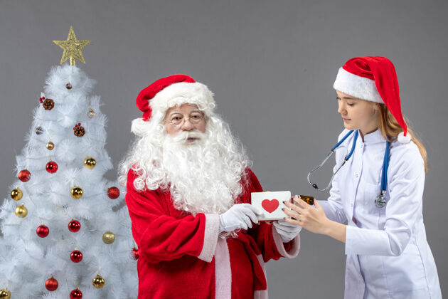 烧瓶圣诞老人和女医生的前视图 女医生拿着一个装着药片的小瓶子 放在灰色的墙上药丸十二月圣诞老人