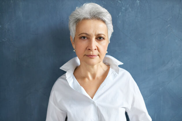 女士自信严肃的成熟女员工的独立肖像 灰色短发皱着眉头在空白墙上摆姿势灰色退休正式
