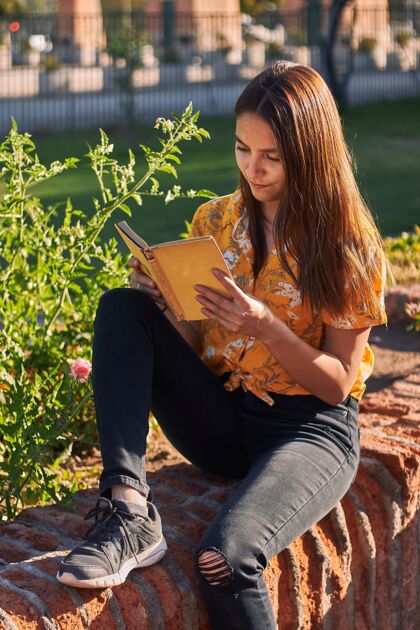 公园一个穿着黄色衬衫的女孩坐在植物旁边看书的垂直镜头树叶读书草