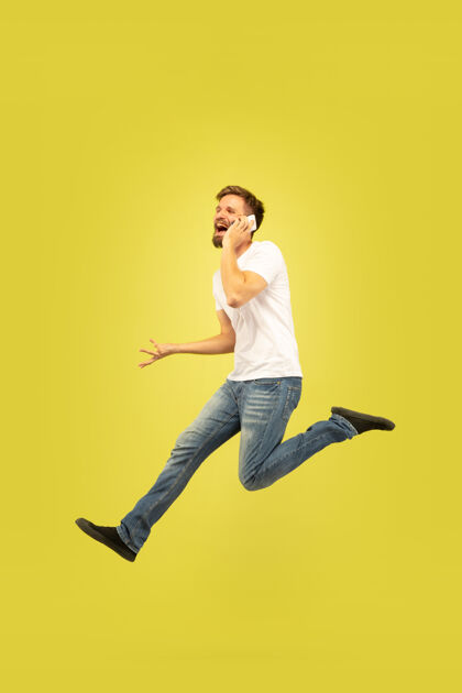 跳跃黄色背景上孤立的快乐跳跃人的全长肖像穿着休闲服的白人男模自由选择 灵感 人类情感概念快点 打电话运动消极休闲