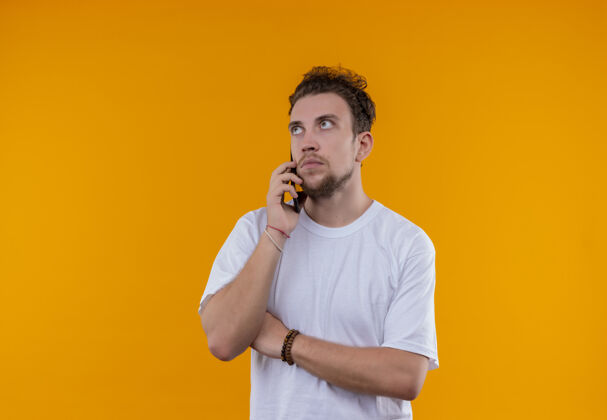 T恤在孤立的橙色背景下 看着穿着白色t恤的年轻人在电话里说话橙色说话看