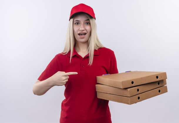 女孩一个穿着红色t恤 戴着牙套帽子的年轻女孩指着她手上的披萨盒 背景是白色的牙科白色支架