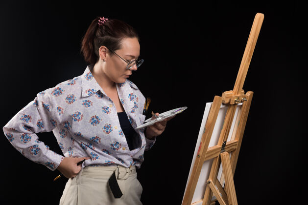 绘画女画家拿着画笔 看着黑色背景上的画布画笔工艺年轻
