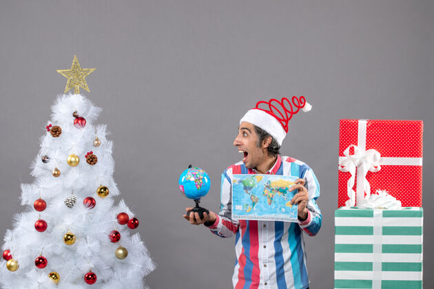 家伙前视图欣喜若狂的男子与螺旋弹簧圣诞帽举行世界地图和地球仪春天圣诞快乐