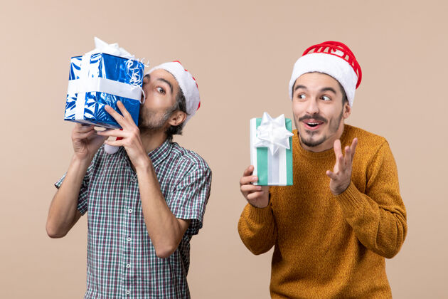 穿着前视图两个兴高采烈的家伙戴着圣诞帽 拿着他们的礼物在孤立的背景男人两个成人