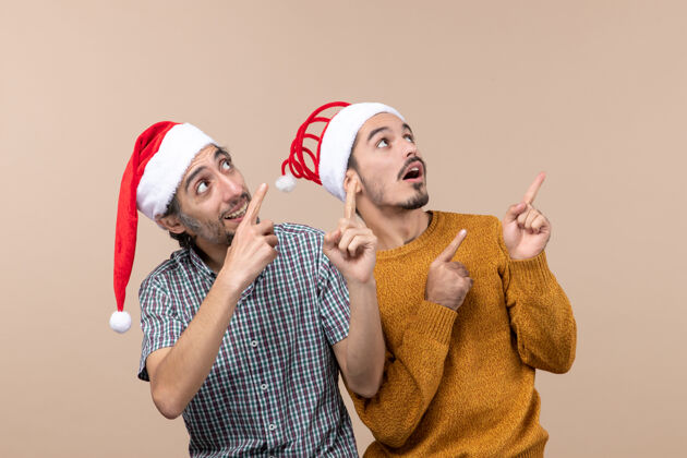 两个正面图：两个戴着圣诞帽的好奇的男人在看一个孤立背景上的东西观点帽子男性