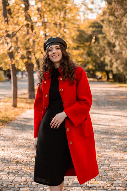 装束迷人的时尚微笑的女人卷发漫步在公园穿着温暖的红色外套秋季时尚 街头风格 戴贝雷帽服装苗条摆姿势