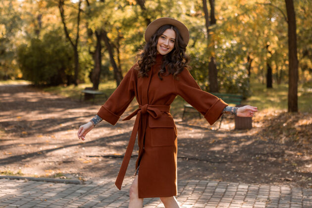 女士迷人时尚微笑的瘦身女子卷发漫步公园身着暖棕色外套 秋日时尚街头风魅力连衣裙波西米亚