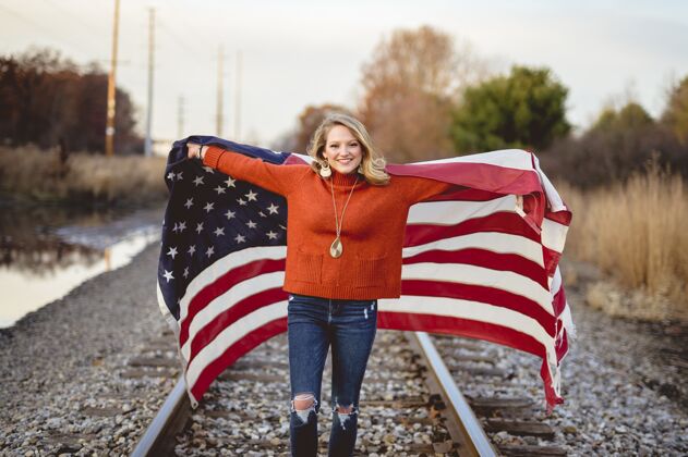 自由站在铁路上手持美国国旗的美丽女性庆典红色团结