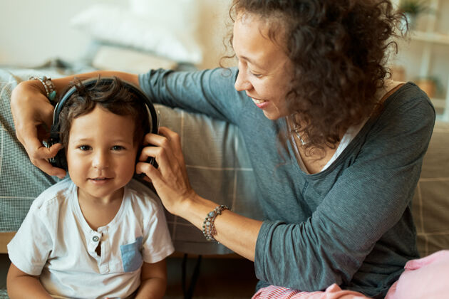 教育年轻的混血妈妈用无线耳机照顾她可爱的三岁儿子耳机女性家长