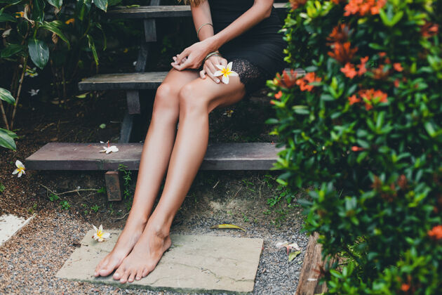 时尚热带花园里年轻漂亮性感的女人 在泰国度暑假 苗条瘦削的棕褐色身材 小黑裙配蕾丝 自然的造型 感性 放松 腿部特写细节晒黑皮肤生活