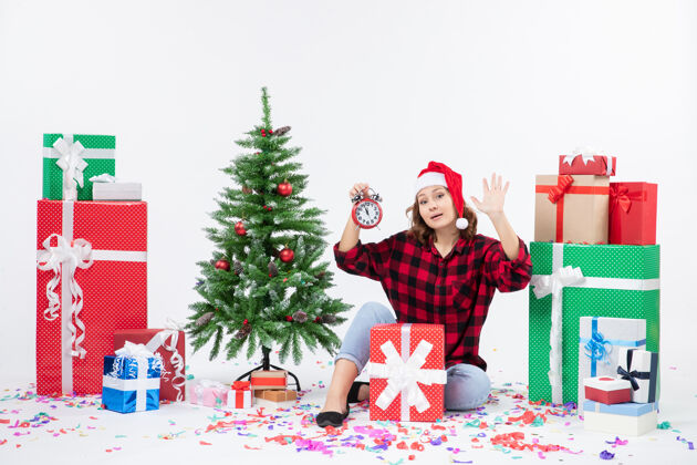 节日前视图年轻女子坐在圣诞礼物周围拿着白色墙上的时钟快乐坐着礼物