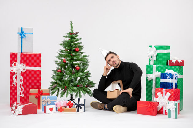 礼物年轻人坐在白色墙壁上的节日礼物周围的正面视图快乐模型微笑