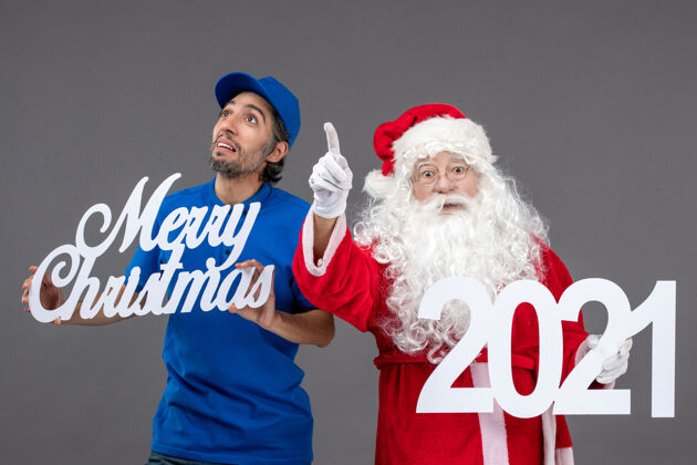 男性圣诞老人的正面图 灰色墙上的男信使手持圣诞快乐和2021年的横幅圣诞老人圣诞老人快乐